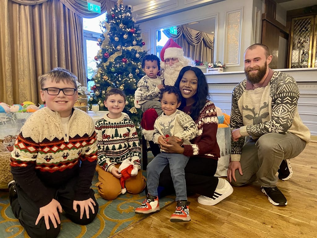 “A festive workplace kids’ Christmas party featuring children dancing, meeting Santa, and enjoying face painting, with cheerful holiday decorations and families mingling in a relaxed setting.