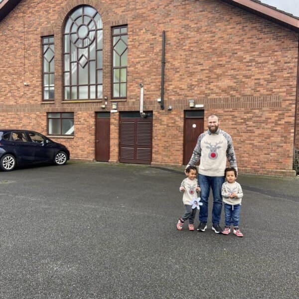 A family standing outside a church in the Irish countryside, dressed in winter outfits, smiling after a Christmas service