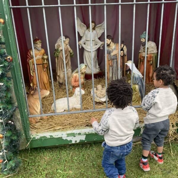 Two young children standing in awe, gazing at a nativity scene with twinkling lights in the background.