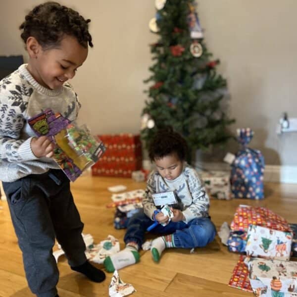 Two smiling children excitedly opening Christmas presents in a cozy living room.